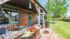 Una casa di legno con un portico, un tavolo e delle sedie, e un'aiuola fiorita.