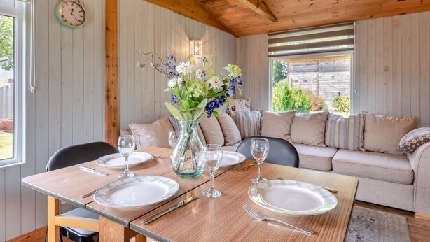 Zona pranzo con tavolo in legno apparecchiato per quattro persone, divano e un vaso di fiori.