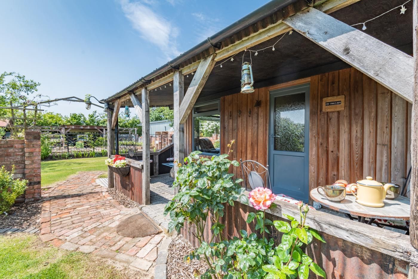 Ein rustikales Holzgebäude mit überdachter Veranda, einem Ziegelweg und einem Gartenbereich mit Blumen und Pflanzen.