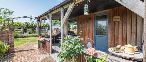 Ein rustikales Holzgebäude mit überdachter Veranda, einem Ziegelweg und einem Gartenbereich mit Blumen und Pflanzen.