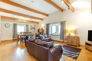 A spacious living room with a leather sofa, wooden flooring, a dining area with a table and chairs, and a television on a wooden cabinet. - 2 Bed in Cowling (oc-ds238) (Cowling)