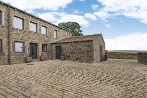 Un bâtiment en pierre avec une petite dépendance attenante, une cour pavée et une vue sur la campagne.