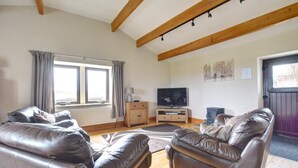 Ein Wohnzimmer mit Ledersofas, einem Fernseher, Holzbalken und einem Fenster mit Vorhängen.
