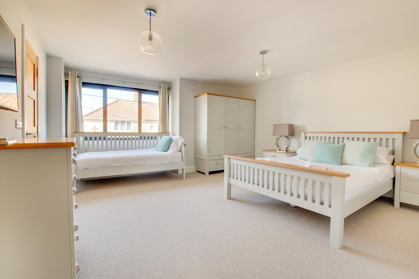 A bedroom with a bed, a daybed, a wardrobe, and a desk with a lamp.