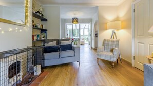 Een woonkamer met een bank, een geruit fauteuil, een lamp en een open haard.