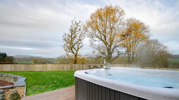 Ein Whirlpool auf einer Holzterrasse mit Blick auf Bäume und Hügel im Hintergrund.