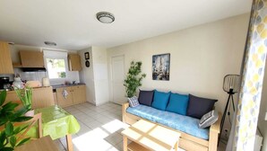 Ett kompakt bostadsutrymme med ett litet kök, en soffa, ett matbord och en golvlampa.