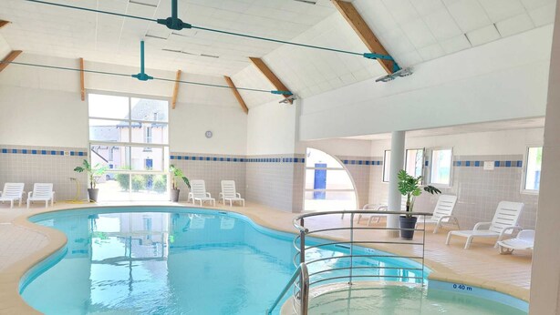 En inomhuspool med klart vatten, omgiven av solstolar och krukväxter.
