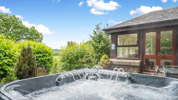 A hot tub with a stone exterior, surrounded by lush greenery and a clear blue sky. - 2 Bed in Methven (oc-c32362) (Methven)