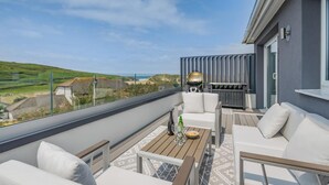 Ein Balkon mit einer Couch, einem Tisch und einem Grill mit Blick auf eine Küstenlandschaft.