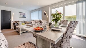 Ein modernes Wohnzimmer mit Essbereich, ausgestattet mit einer Sofagarnitur, einem Couchtisch mit Obst und Blick ins Freie.