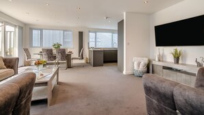 Ein geräumiges Wohnzimmer mit einer Couch, einem Couchtisch und einem an der Wand montierten Fernseher.