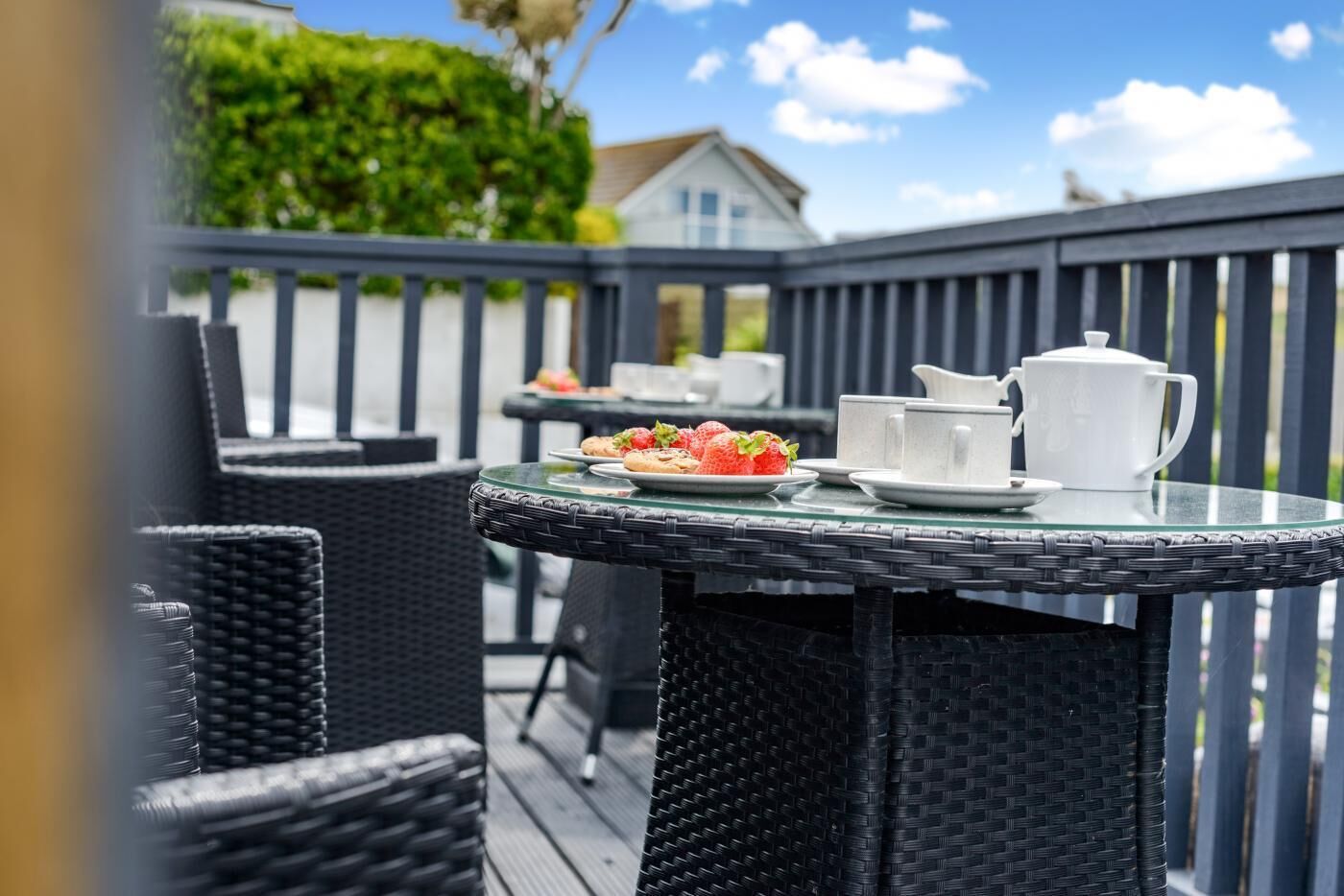 Ein Essbereich im Freien aus Rattan mit Tisch für zwei Personen, gedeckt mit Geschirr, Speisen, einer Karaffe und Tassen.