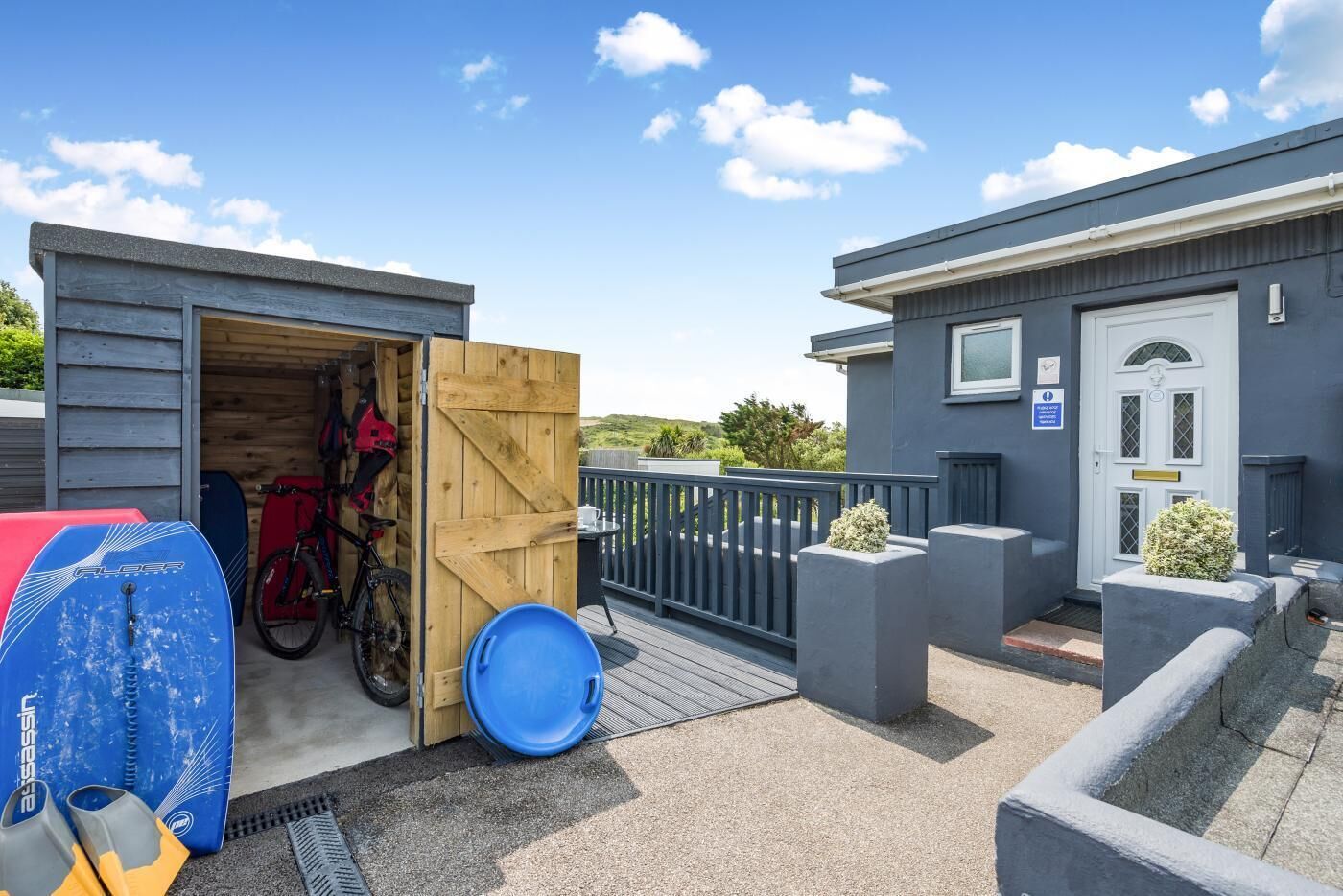A covered outdoor area with a wooden door, a bicycle, and a blue barrel.