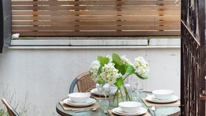 A round glass table set with white plates, bowls, and cutlery, surrounded by wicker chairs, with a wooden fence and a brick wall in the background. - 2 Bed in Whitby (oc-w003) (Whitby)