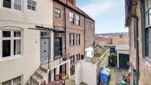 A narrow alleyway between two buildings with a small garden area, a blue trash bin, and a green recycling bin. - 2 Bed in Whitby (oc-w003) (Whitby)
