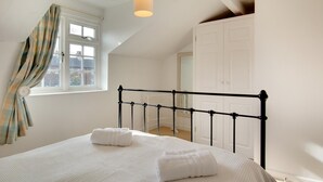 Ein Schlafzimmer mit Bett, einem Fenster mit Vorhängen, einer Hängelampe und einem Kleiderschrank.