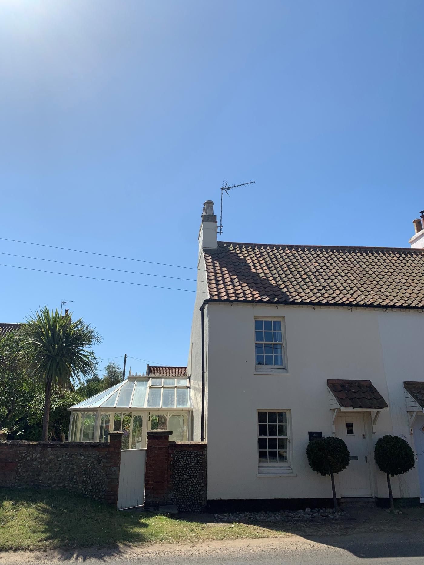 A two-story house with a tiled roof, a conservatory, and a small garden with a palm tree.