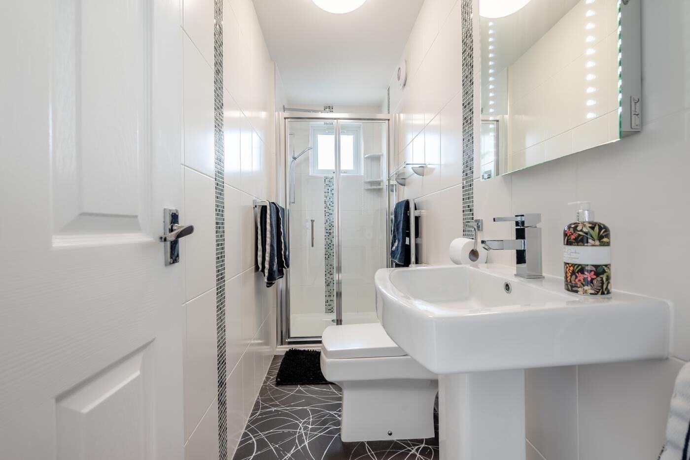 Une salle de bain moderne avec un lavabo blanc, une douche en verre et un sol carrelé.
