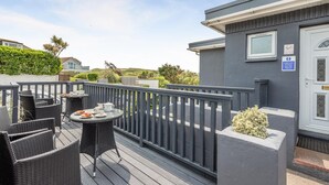 A balcony with wicker furniture and a table set for dining, surrounded by a grey railing. - 1 Bed in Newquay (oc-o32401) (Holywell)