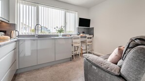 A modern kitchen with a large window, a dining area with a table and chairs, and a grey sofa. - 1 Bed in Newquay (oc-o32401) (Holywell)