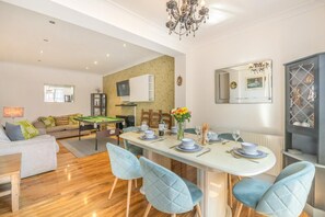Ein modernes Wohnzimmer mit Billardtisch, einem Essbereich mit langem Tisch für vier Personen und einer Küche im Hintergrund.