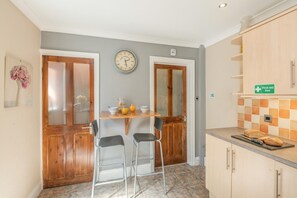 A kitchen with a wooden table, two chairs, a clock, and a first aid box sign. - 6 Bed in Scarborough (oc-s871) (Scarborough)