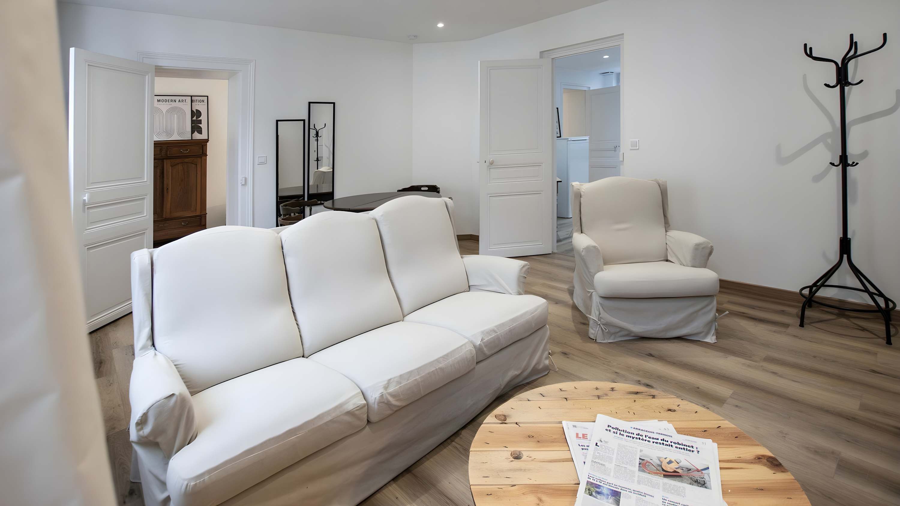 Una sala de estar moderna con un sofá de cuero blanco, un sillón a juego y una mesa de centro de madera con periódicos.