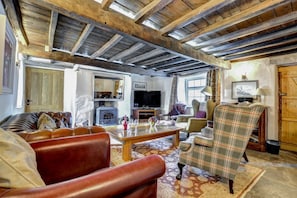 A rustic living room with exposed wooden beams, a fireplace, leather sofas, and a plaid armchair. - 3 Bed in Sedbergh (oc-ds169) (Garsdale)
