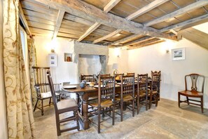 A rustic dining room with a wooden table and chairs, stone flooring, and exposed wooden beams on the ceiling.