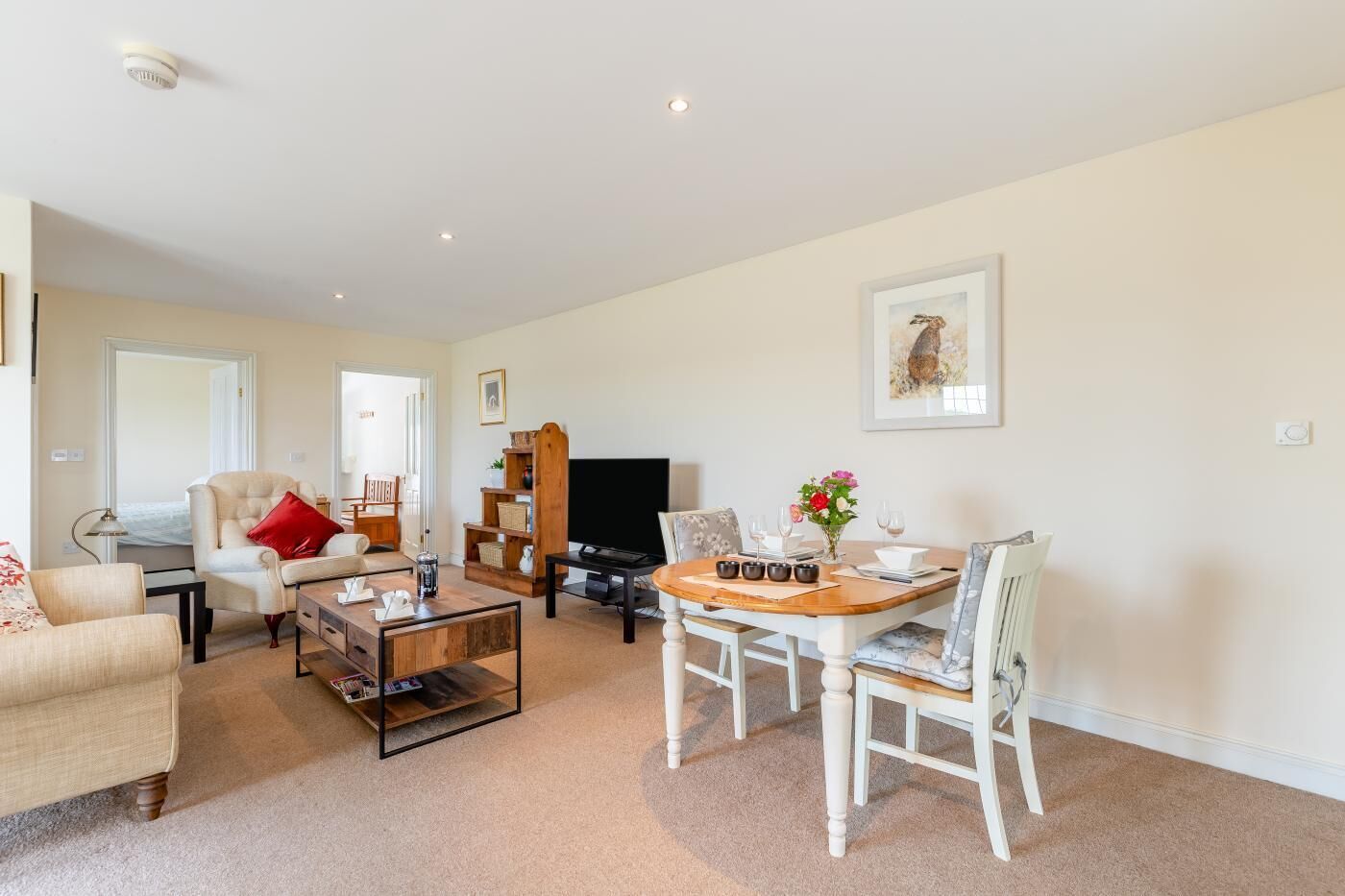 A living room with a sofa, armchair, coffee table, TV, and a dining table with chairs.