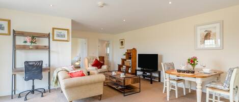 A living room with a sofa, armchairs, a coffee table, a TV, and a dining table with chairs.