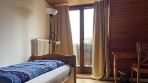 Ein Schlafzimmer mit einem hölzernen Bett, einem Schreibtisch, einem Stuhl und einem Fenster mit Vorhängen.