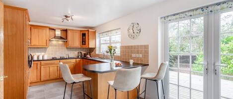 A modern kitchen with wooden cabinets, a central island with bar stools, a large window, and a clock on the wall.