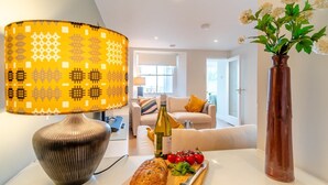 Uma sala de estar moderna com uma luminária estampada, uma garrafa de vinho, tomates e um pão sobre uma mesa.