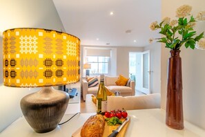 A modern living room with a patterned lamp, a bottle of wine, tomatoes, and a loaf of bread on a table. - 3 Bed in Tenby (oc-p32426) (Tenby)