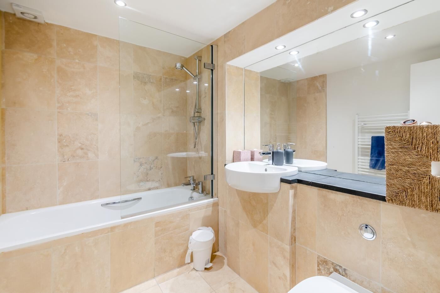 A modern bathroom with a bathtub, two sinks, a shower, and a large mirror.