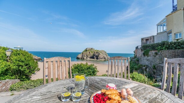 Uma mesa com uma refeição, vista para o mar e um afloramento rochoso ao longe.