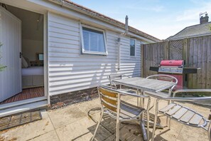 A mobile home with a patio area featuring a metal table and chairs, a grill, and a small enclosed space with a bed.