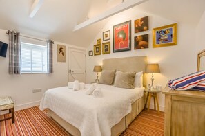 A hotel room with a bed, bedside lamps, a TV mounted on the wall, and a window with curtains.