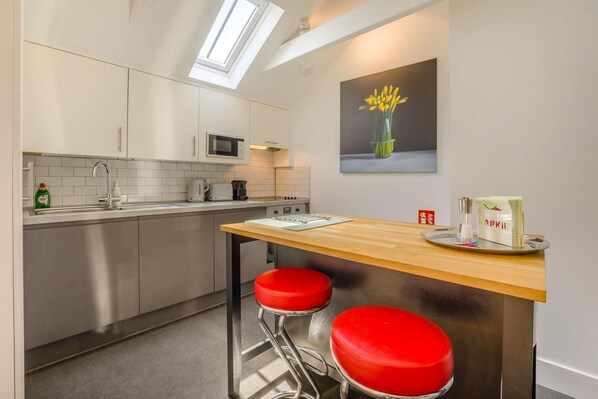 A modern kitchen with a skylight, stainless steel appliances, and a bar area with red stools.