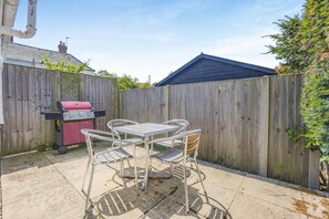 A backyard with a barbecue grill, a metal table with chairs, and a wooden fence.