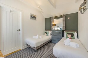 A hotel room with two beds, a dresser, a window with curtains, a door, and a small picture on the wall.