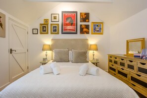 A hotel room with a large bed, two bedside tables with lamps, a wooden dresser, and a wall decorated with framed pictures and a poster.