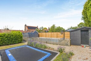 A residential backyard with a trampoline, a wooden fence, a shed, and a house with a sloped roof.