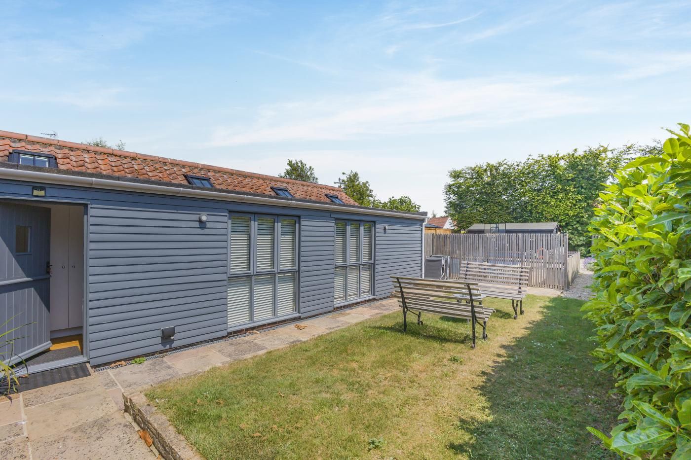 A single-story building with a grey exterior, a tiled roof, and a fenced backyard.