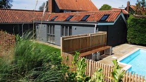 Ett modernt hus med en swimmingpool, ett trädäck och en inhägnad trädgårdsyta.