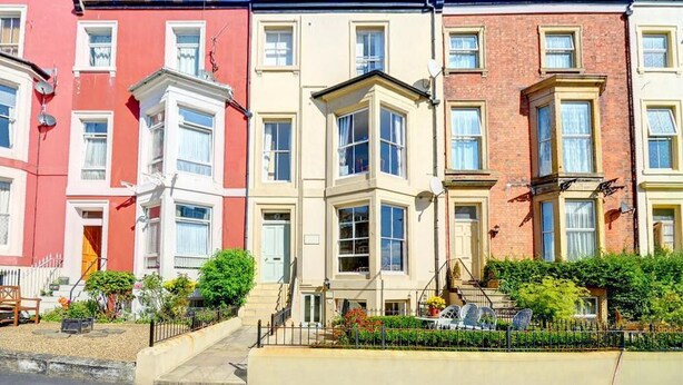 A row of terraced houses with bay windows, a front garden, and a clear blue sky. - 2 Bed in Whitby (oc-w979) (Whitby)