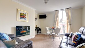 A living room with a sofa, a TV, a fireplace, and a dining area with chairs and a table. - 2 Bed in Whitby (oc-w979) (Whitby)