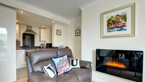 A living room with a brown leather sofa, a fireplace, and a kitchen in the background. - 2 Bed in Whitby (oc-w979) (Whitby)